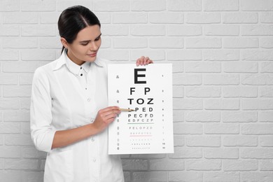 Photo of Ophthalmologist pointing at vision test chart near white brick wall, space for text