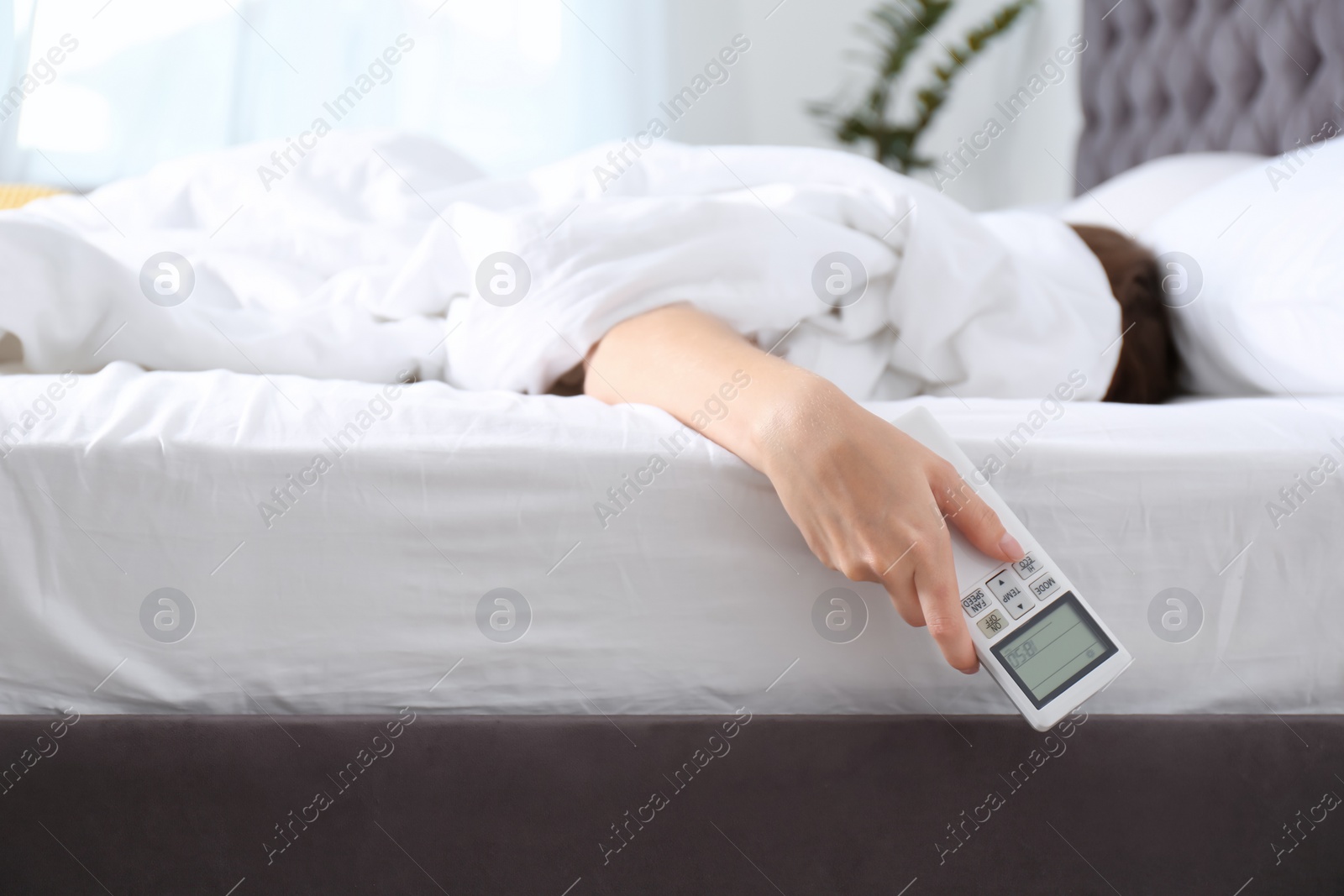 Photo of Woman holding air conditioner remote control in bed, focus on hand