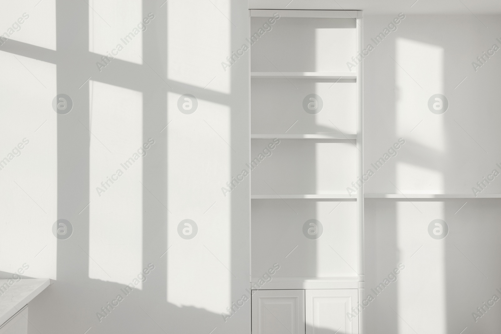 Photo of Light and shadows from window on wall and shelving unit indoors