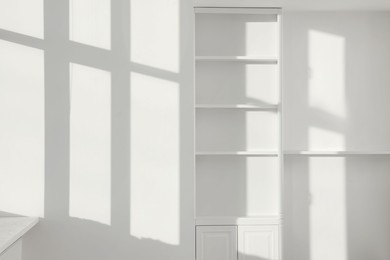 Light and shadows from window on wall and shelving unit indoors