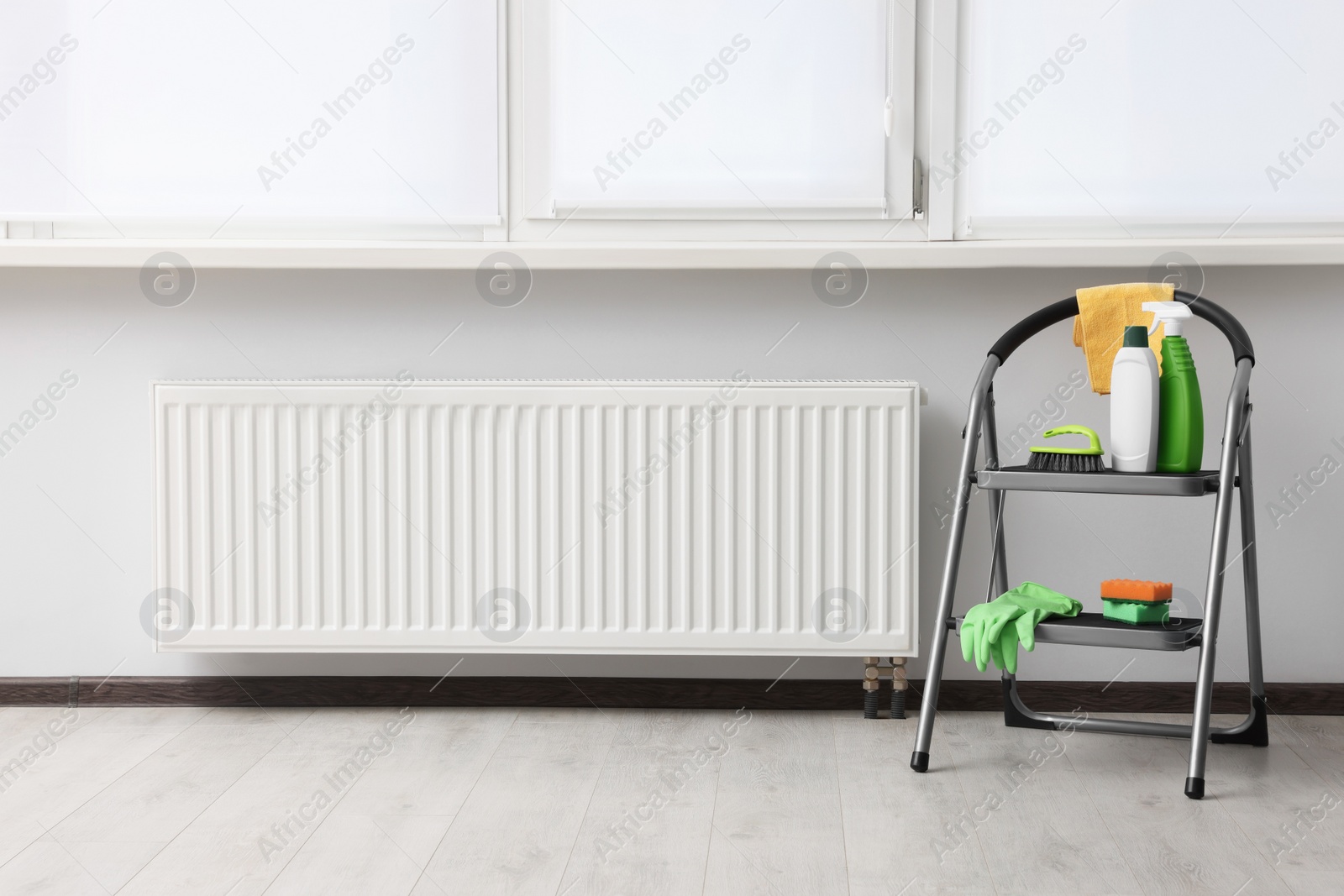 Photo of Ladder with cleaning supplies near modern radiator in room