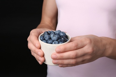 Photo of Woman holding crockery with juicy fresh blueberries in hands, closeup view