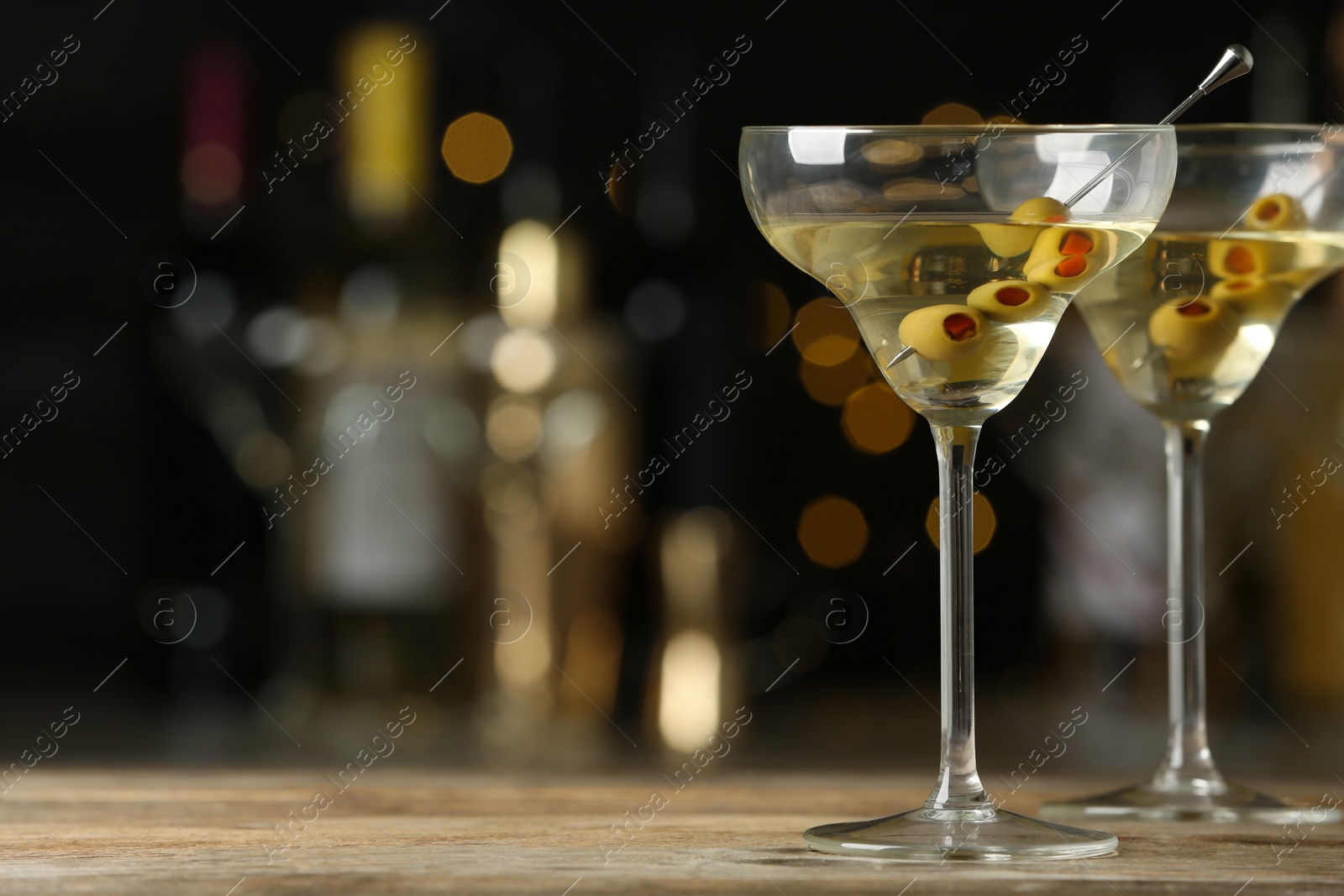 Photo of Glasses of Classic Dry Martini with olives on wooden table against blurred background. Space for text