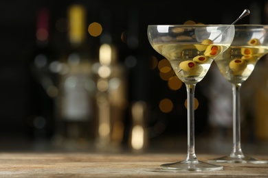 Glasses of Classic Dry Martini with olives on wooden table against blurred background. Space for text