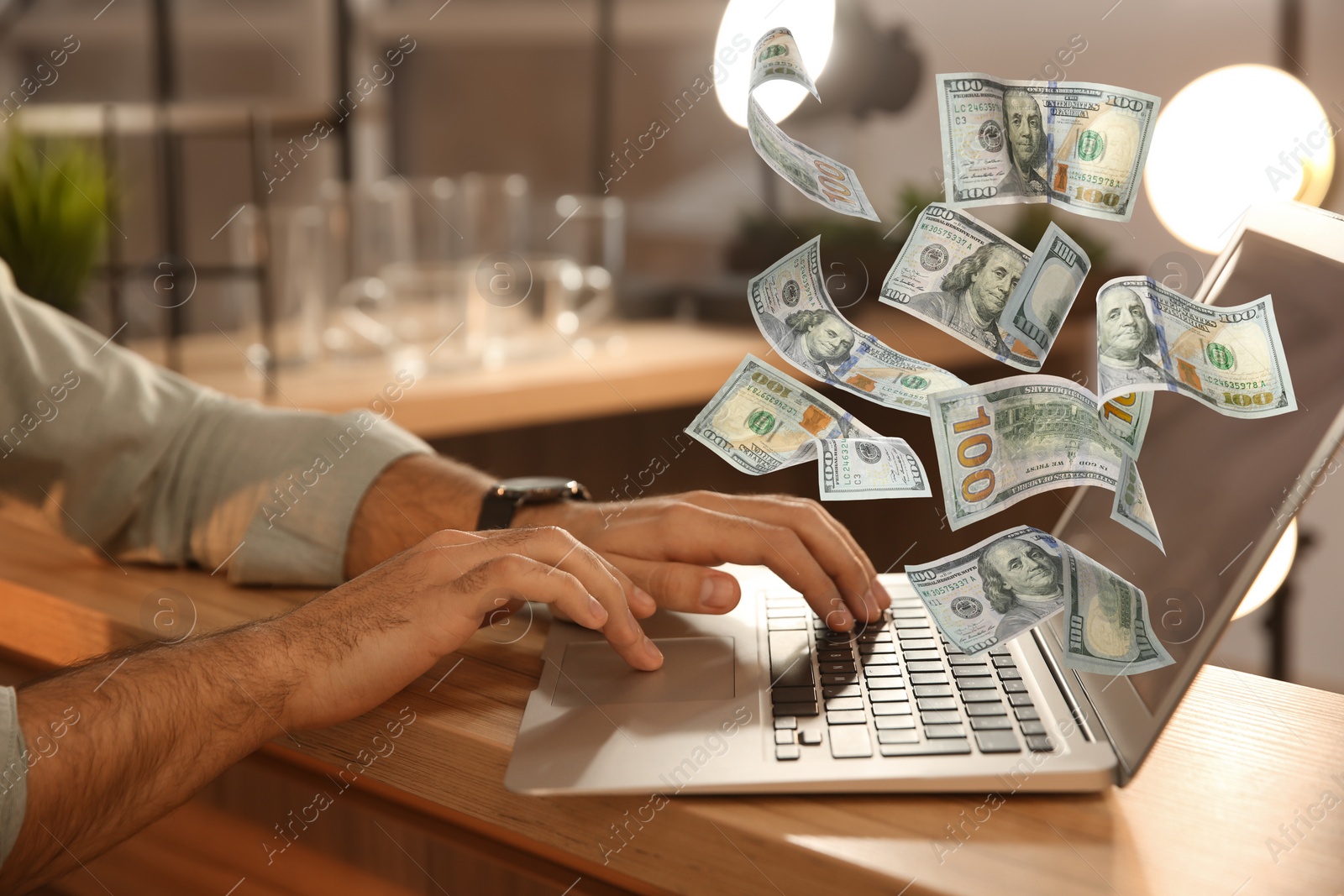 Image of Making money online. Closeup view of man using laptop at table and flying dollars