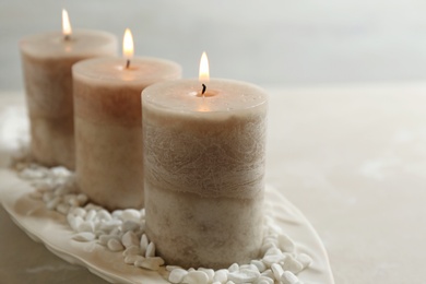 Photo of White plate with three burning candles and rocks on table, space for text