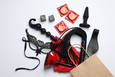 Shopping bag and different sex toys on white background, flat lay