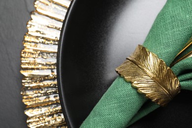 Photo of Green fabric napkin and decorative ring for table setting on black plate, top view