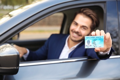 Young man holding driving license in car. Space for text