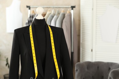 Photo of Mannequin with black jacket and measuring tape in tailor shop, space for text