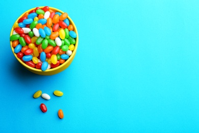 Bowl with colorful jelly beans on turquoise background, flat lay. Space for text
