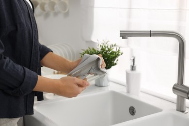 Woman wiping glass with towel in kitchen, closeup