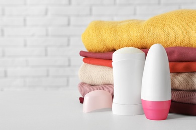 Photo of Deodorants near stack of clean clothes on white table. Space for text