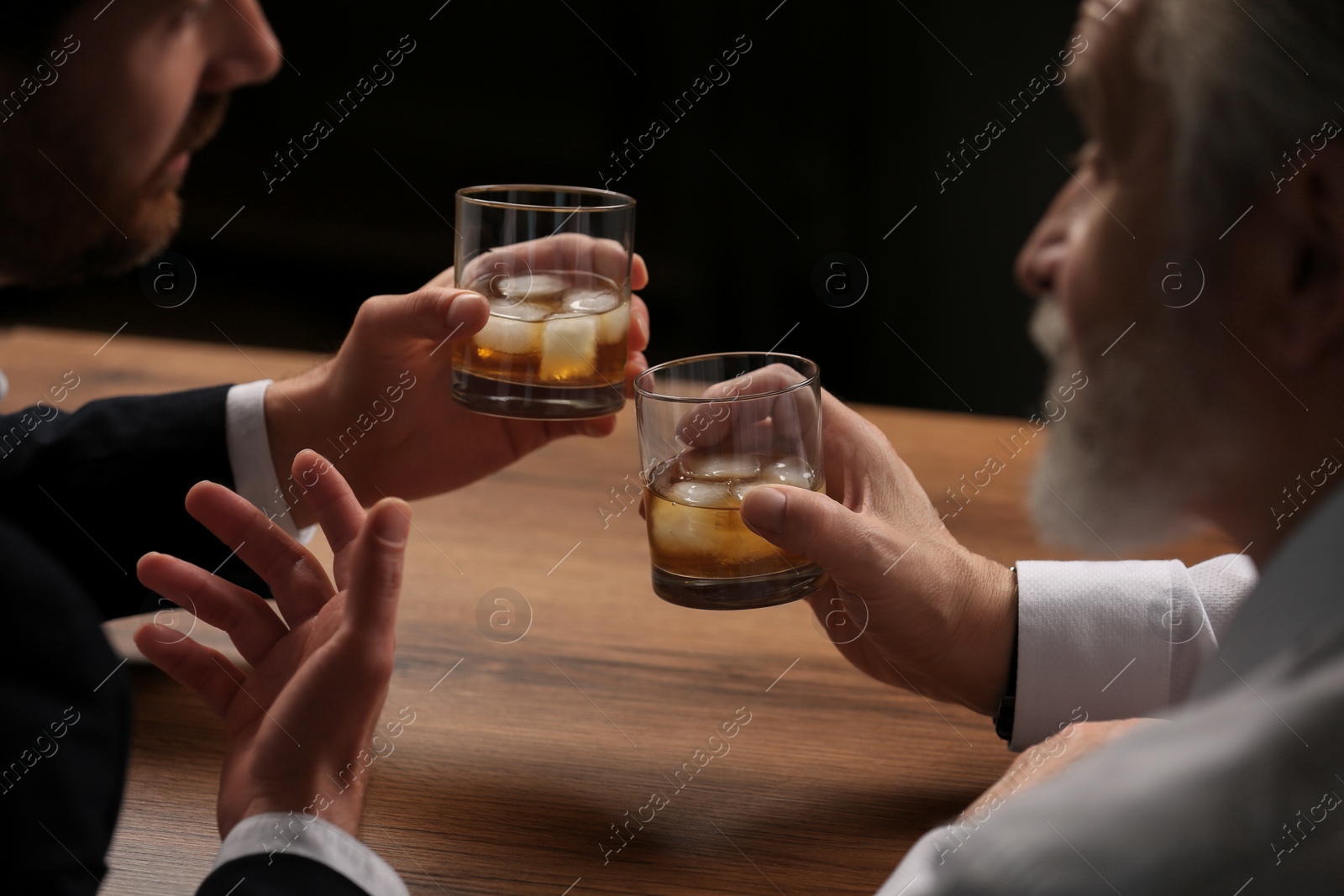 Photo of Men with glasses of whiskey talking at wooden table in bar