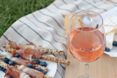 Glass of delicious rose wine and food on picnic blanket outdoors, closeup