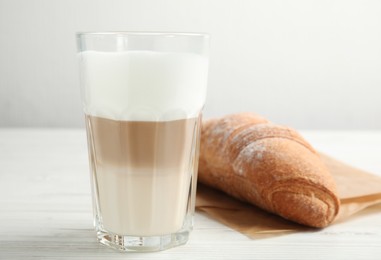 Photo of Delicious latte macchiato and croissant on white wooden table
