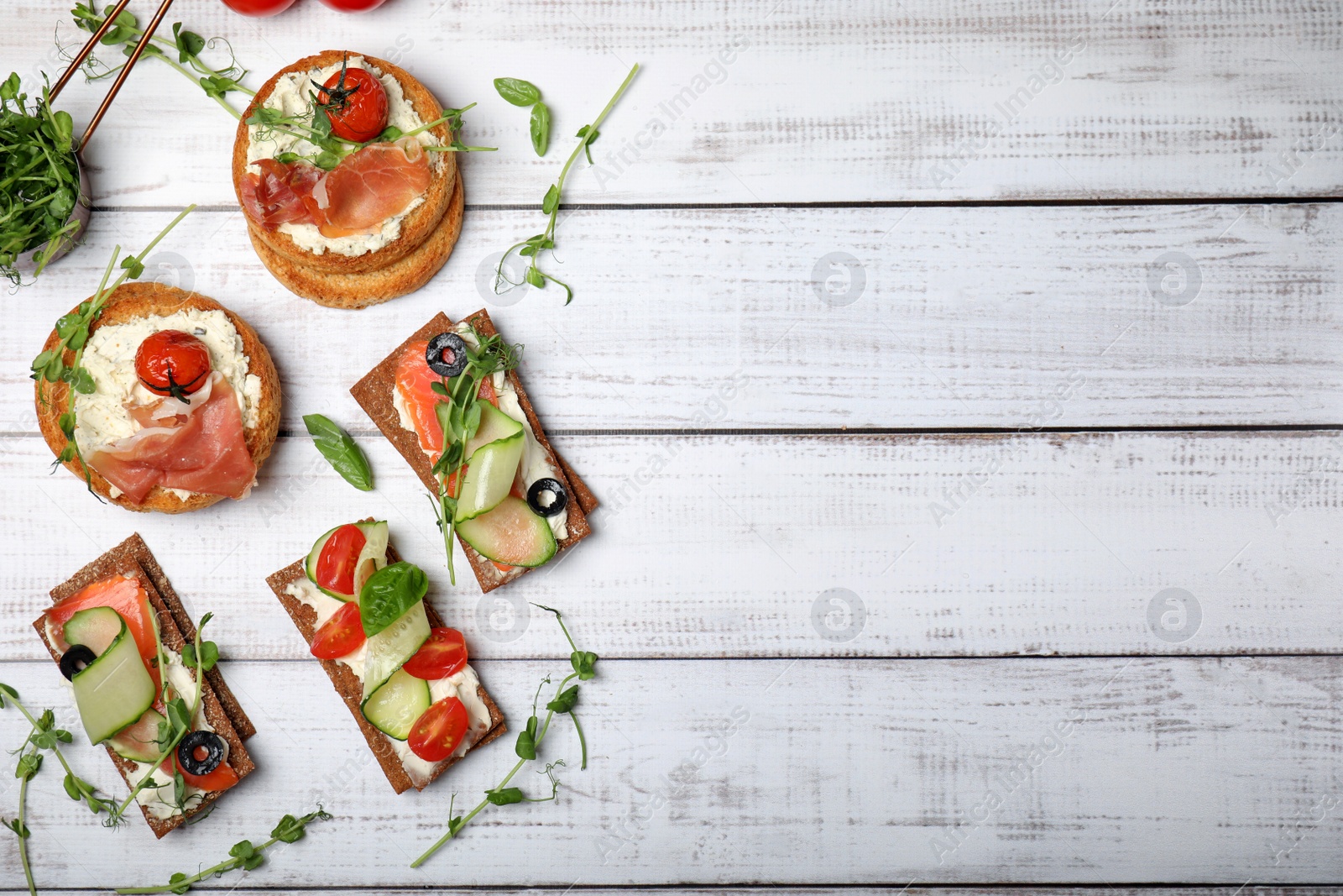 Photo of Tasty rusks and rye crispbreads with different toppings on white wooden table, flat lay. Space for text