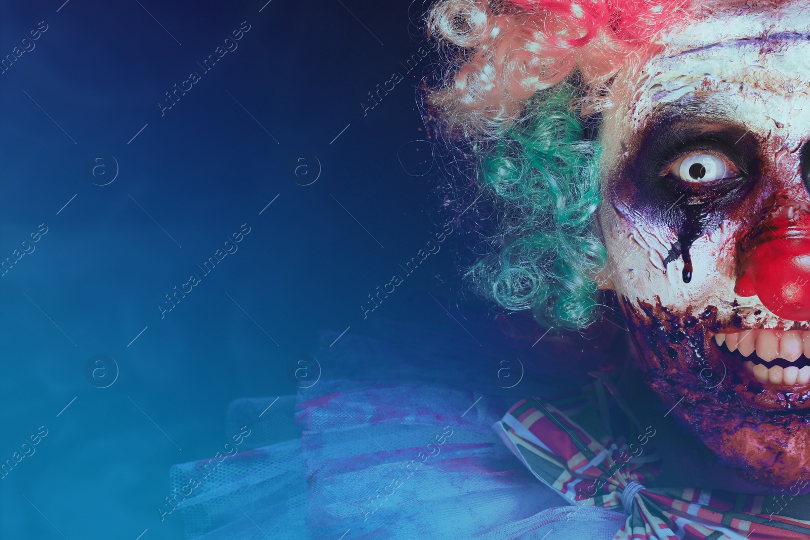 Photo of Terrifying clown on dark background, closeup with space for text. Halloween party costume