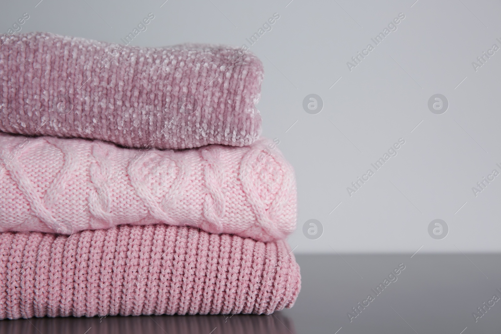 Photo of Stack of folded knitted sweaters on grey table, closeup. Space for text