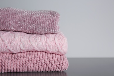 Photo of Stack of folded knitted sweaters on grey table, closeup. Space for text