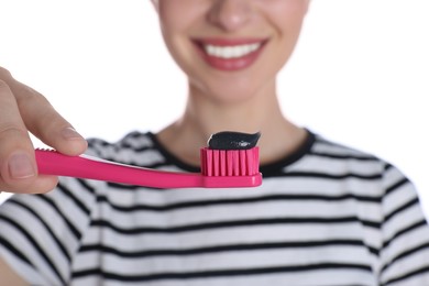 Photo of Woman holding brush with charcoal toothpaste on white background, closeup
