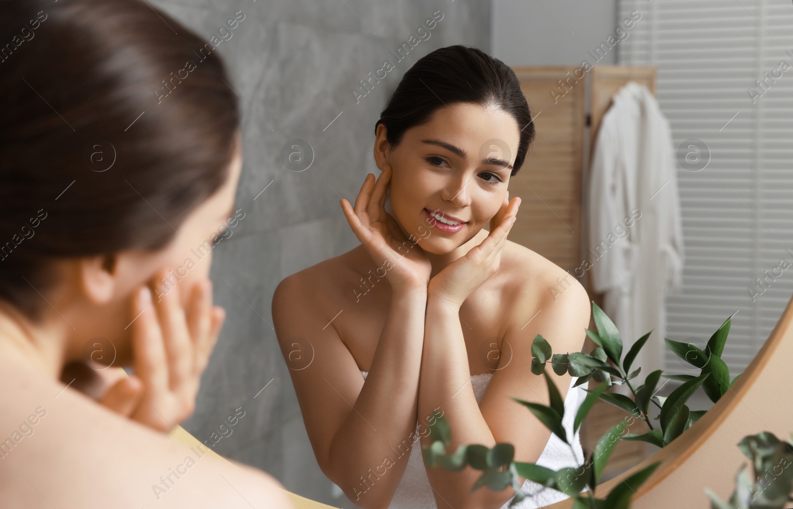 Photo of Young woman massaging her face near mirror in bathroom