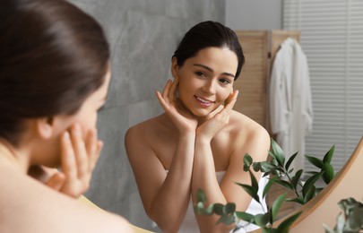 Young woman massaging her face near mirror in bathroom