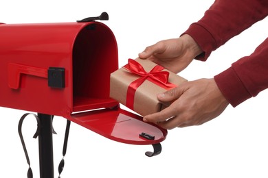 Man putting Christmas gift into mailbox on white background, closeup. Sending present by mail