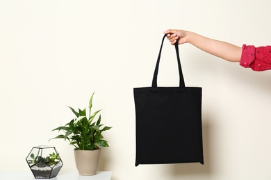 Photo of Woman with stylish blank eco bag  near white wall, closeup. Space for text