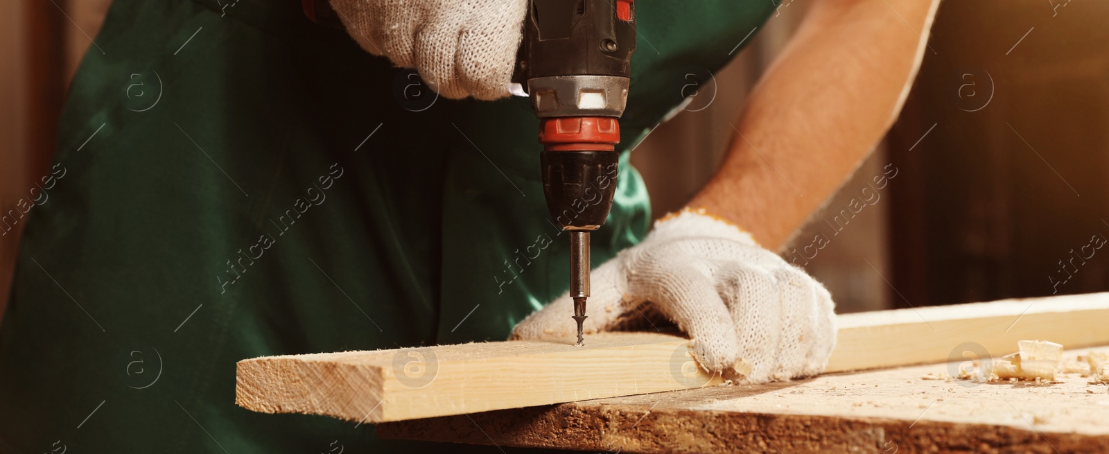 Image of Professional carpenter twisting screw into wooden plank with drill in workshop, closeup. Banner design