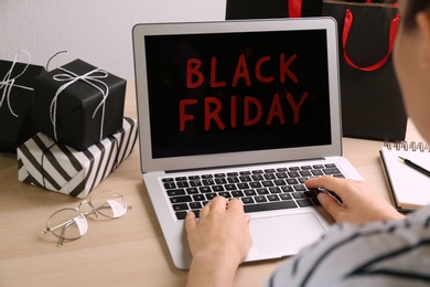 Woman using laptop with Black Friday announcement at wooden table, closeup