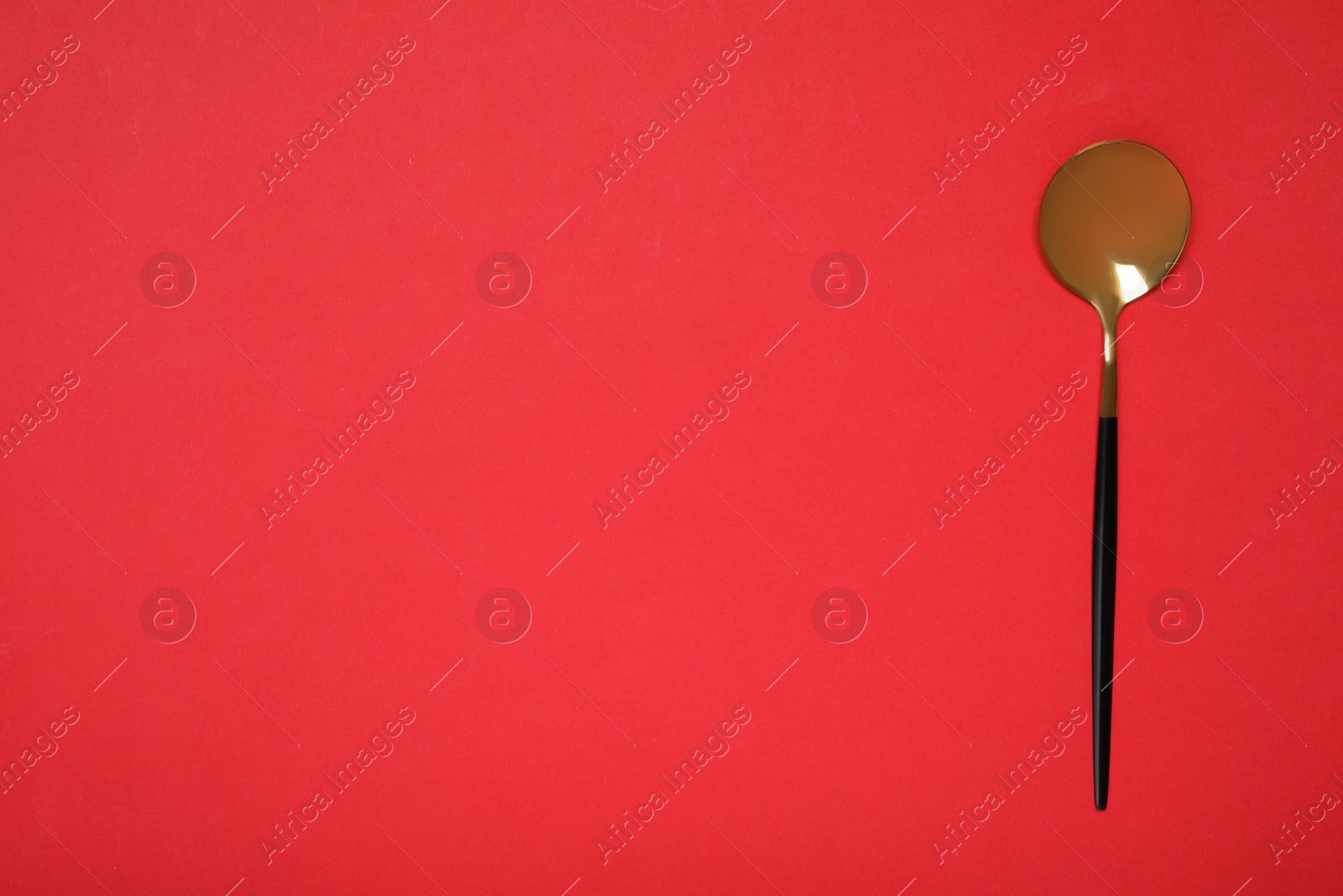 Photo of One shiny golden spoon on red background, top view. Space for text