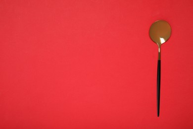 One shiny golden spoon on red background, top view. Space for text