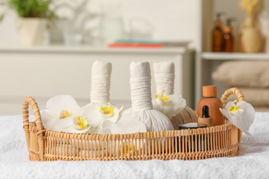 Wicker tray with herbal bags and other spa products on white bath towel