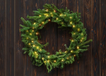 Photo of Beautiful Christmas wreath with festive lights on wooden background, top view