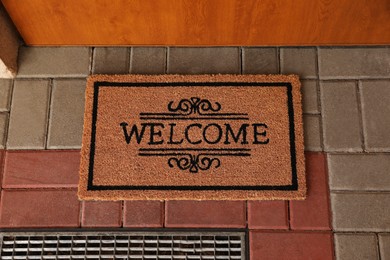 Photo of Door mat with word Welcome on street tiles near entrance, top view