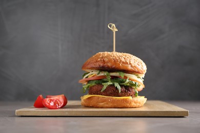 Photo of Board with delicious vegetarian burger on grey table