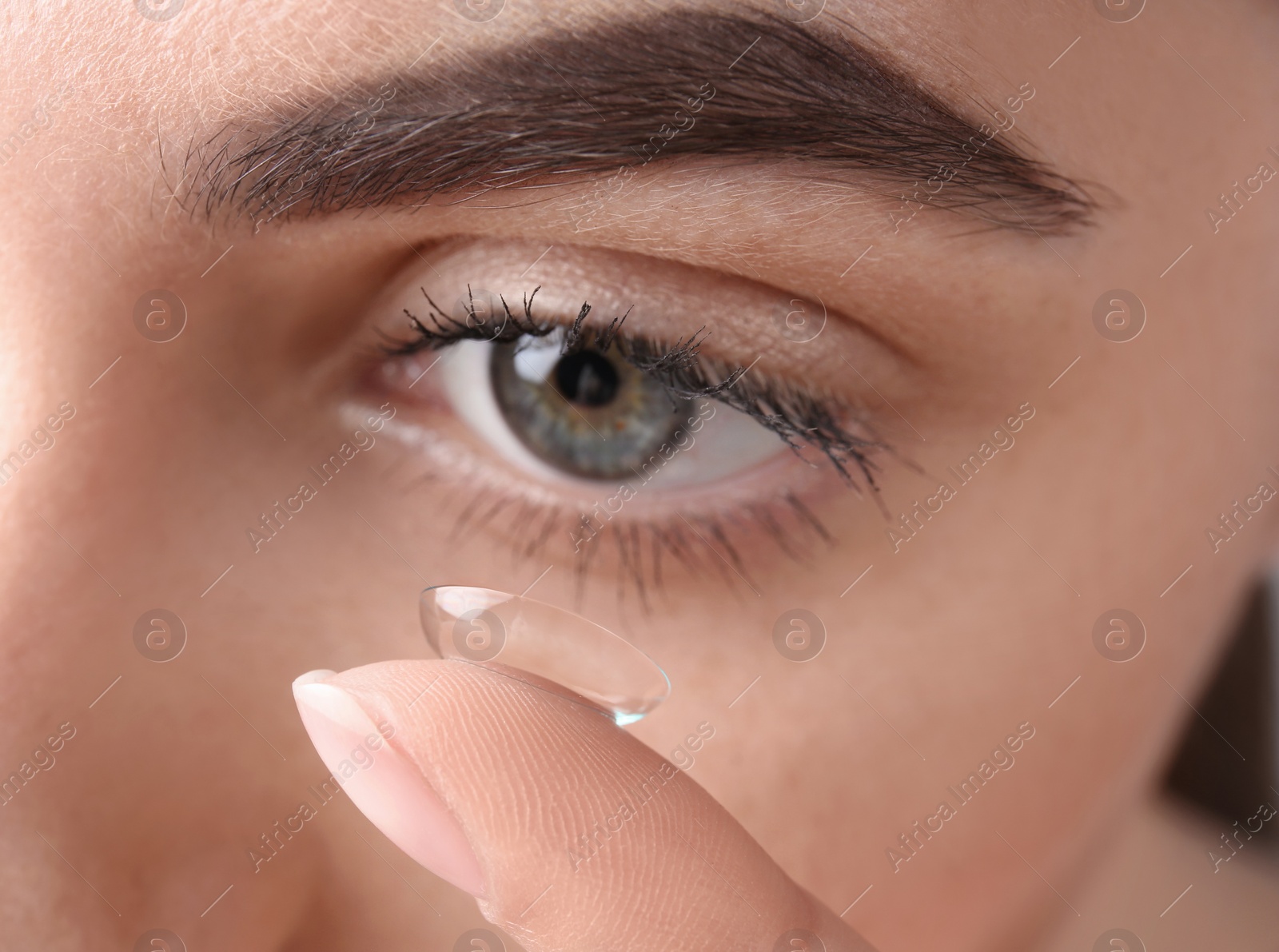 Photo of Young woman putting contact lens in her eye, closeup