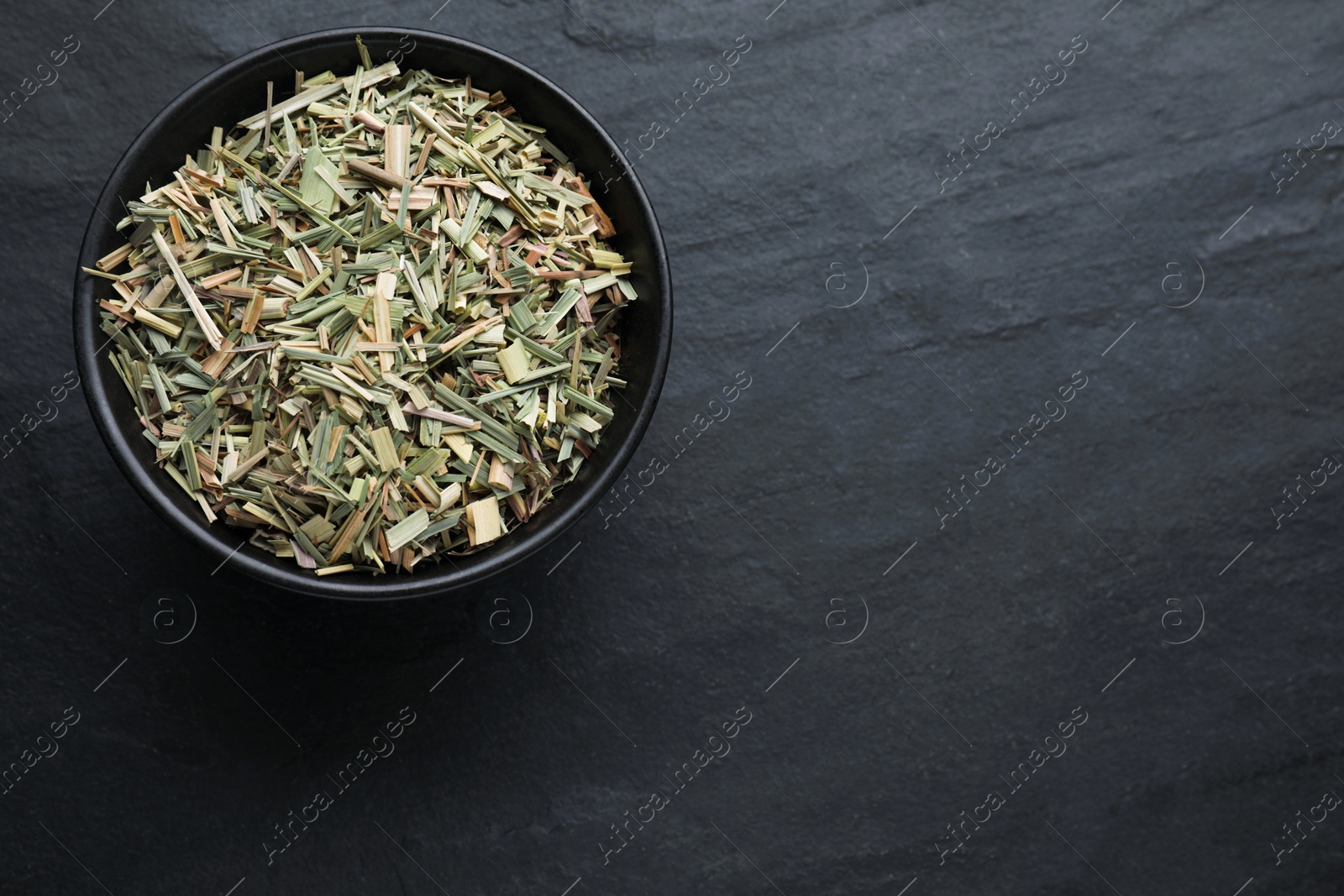 Photo of Bowl with aromatic dried lemongrass on black table, top view. Space for text