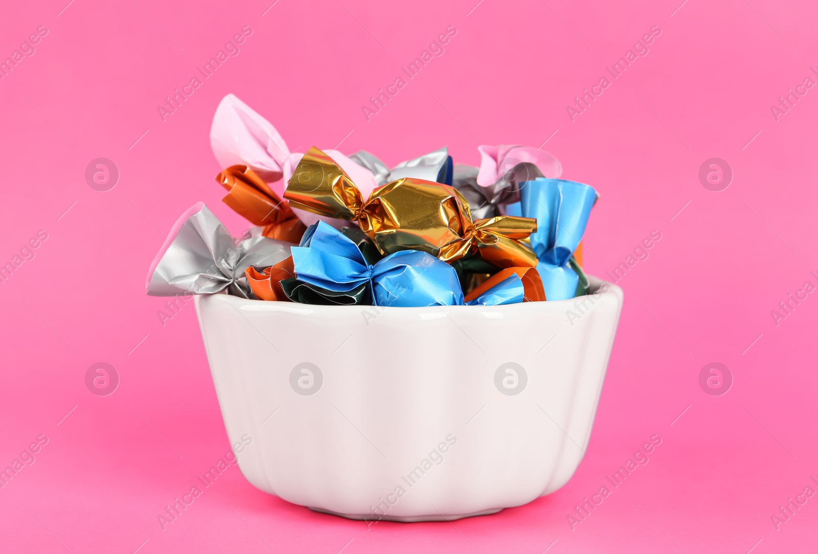 Photo of Candies in colorful wrappers on pink background, closeup