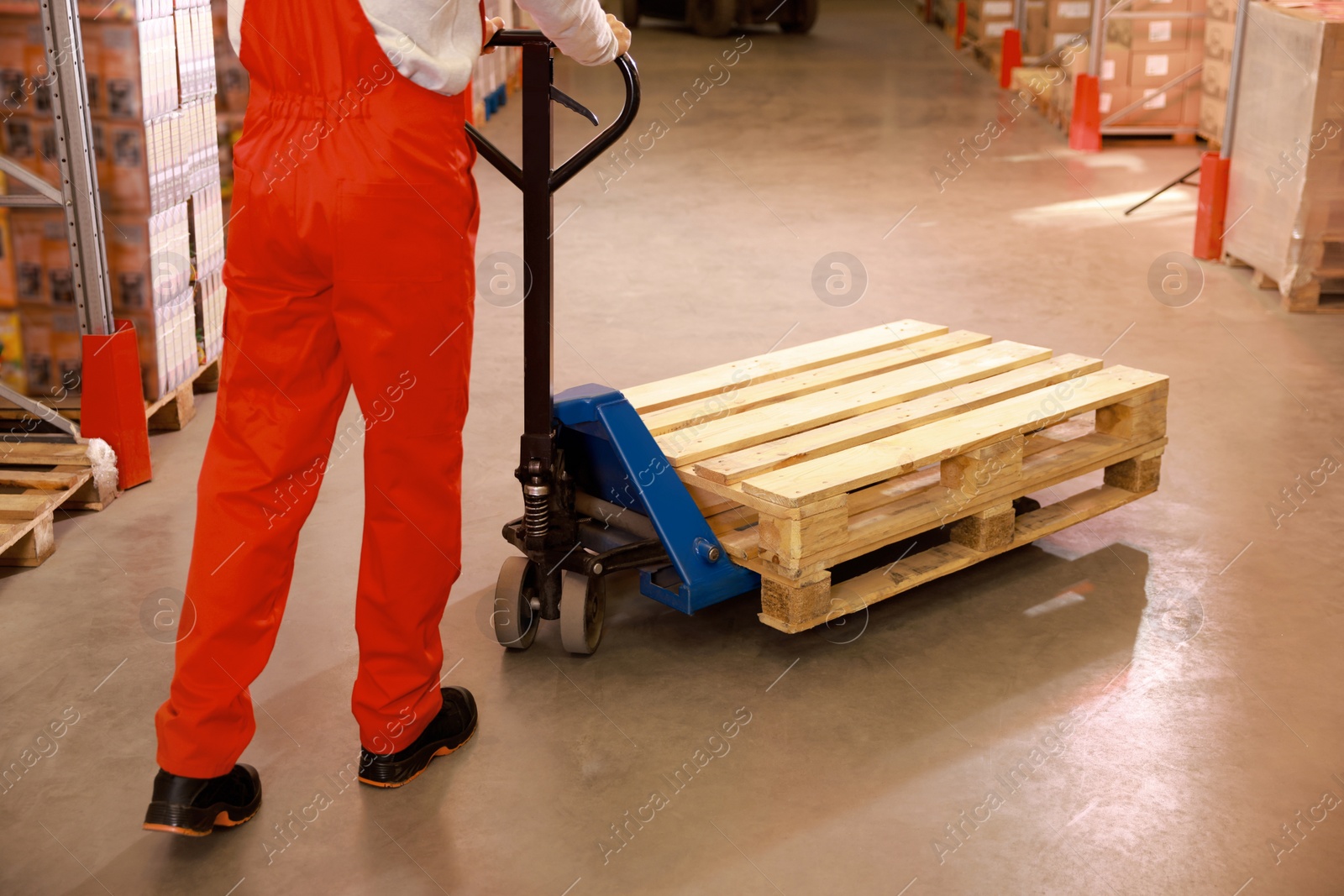 Image of Worker moving wooden pallets with manual forklift in warehouse, closeup