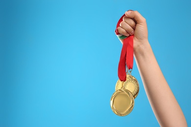 Woman holding gold medals on light blue background, closeup. Space for text