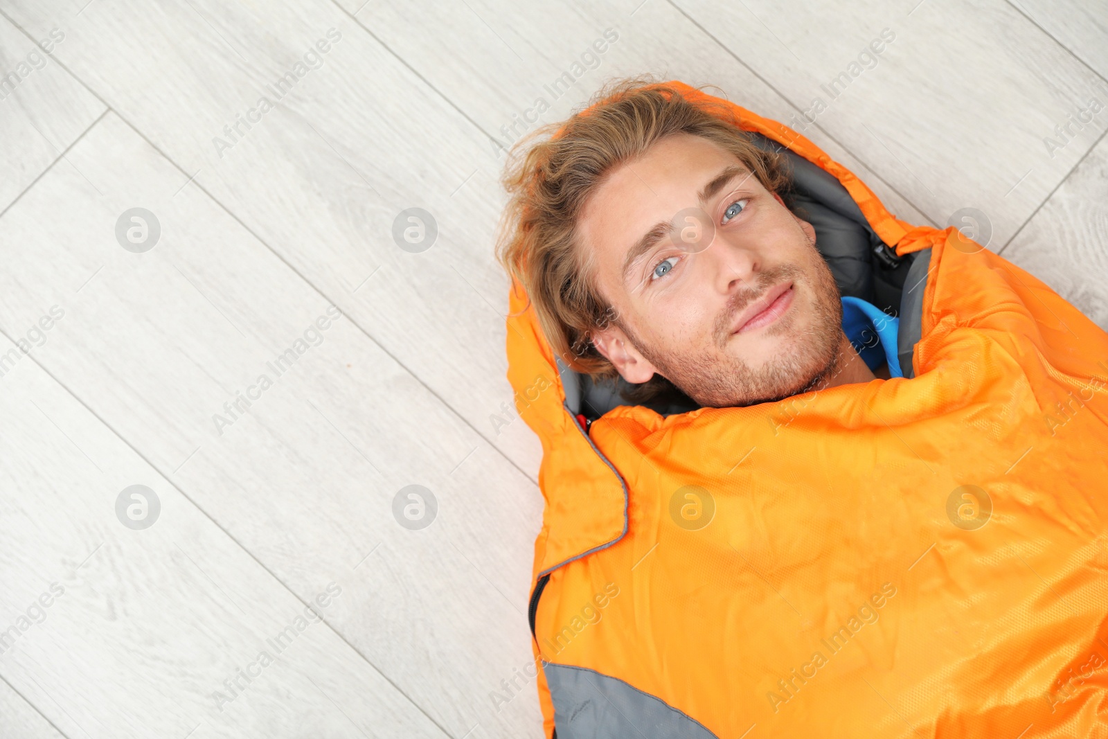 Photo of Young man in comfortable sleeping bag on floor, top view. Space for text