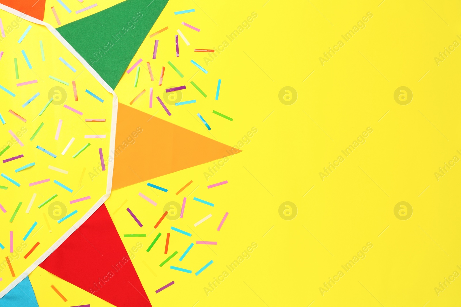 Photo of Bunting with colorful triangular flags and confetti on yellow background, flat lay. Space for text