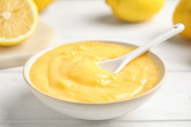 Delicious lemon curd in bowl on white wooden table, closeup