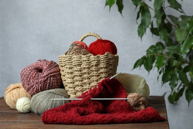 Photo of Soft woolen yarns, knitting and needles on wooden table indoors