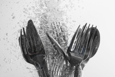 Photo of Washing silver cutlery in water on white background