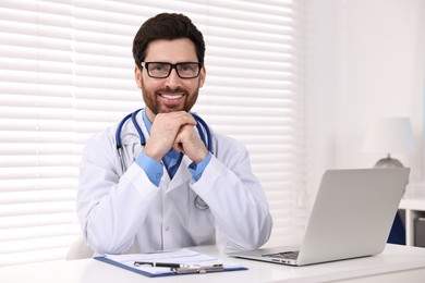 Photo of Medical consultant with glasses and stethoscope at table in clinic