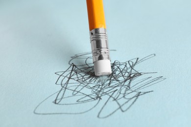 Photo of Erasing scribbles with graphite pencil on light blue background, closeup