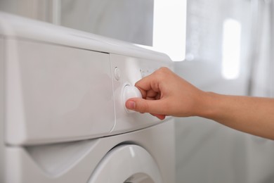 Woman turning on washing machine in bathroom, closeup. Laundry day